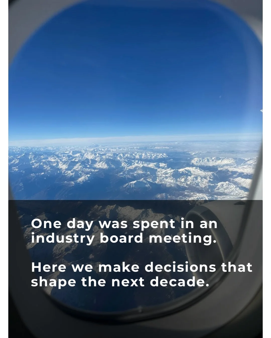 Snow-covered mountains beneath a blue sky, photographed through an aircraft window by Bill