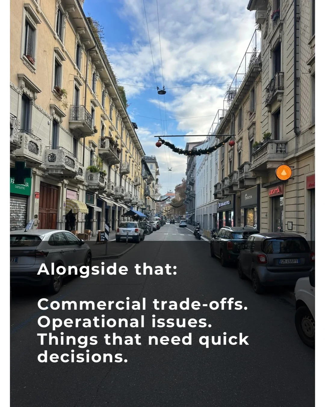 A European street with local shops, stone buildings and blue sky, from Bill’s travels